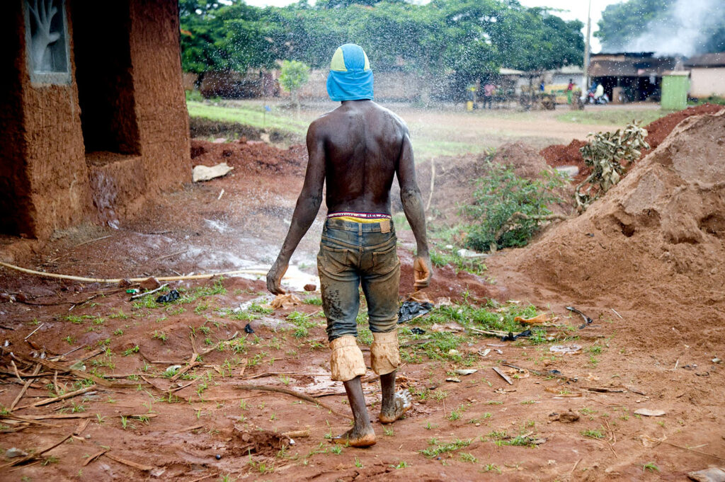 1 homme se tient de dos. Il regarde une canalisation d’eau qui fuie. Scène de rue. Street photographie. Couleurs. François Guibilato photographe.