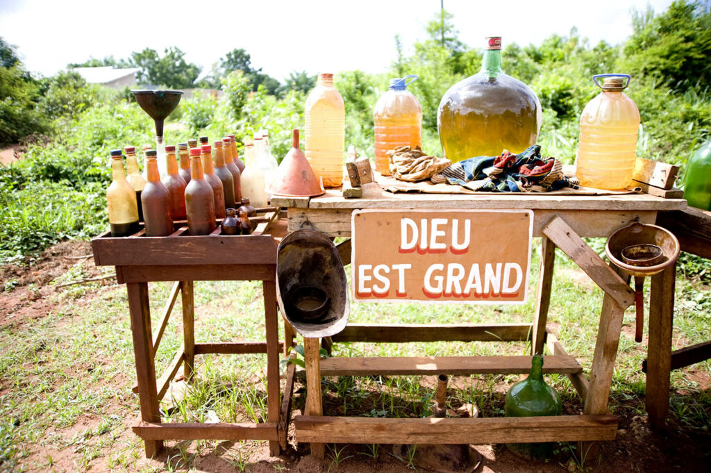 Des bidons d’essence sont présentées dans la rue. Il est écrit sur une affiche Dieu est grand. Abomey. Bénin. François Guibilato photographe.