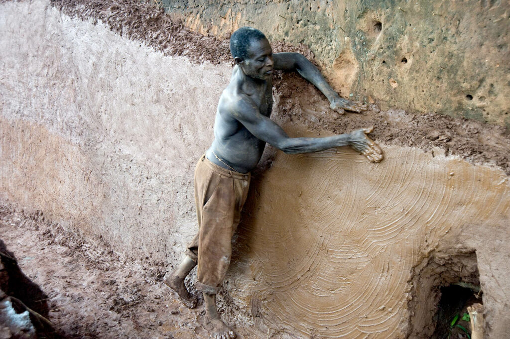 1 homme travaille la terre rouge d'Abomey. Construction. Scène de rue. Street photographie. Couleurs. François Guibilato photographe.