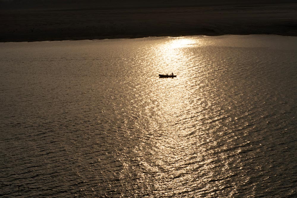 Une barque remonte la rivière Gange. Lever de soleil. Couleurs. Doré. Varanasi. François Guibilato Photographe.