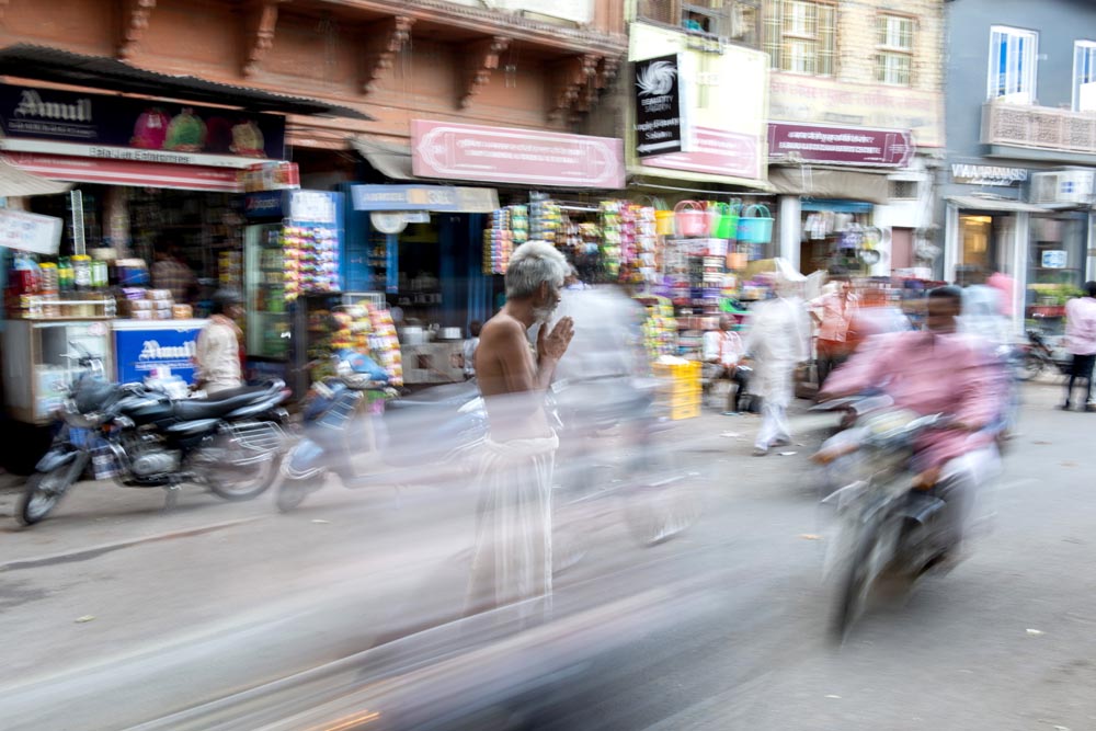 Un homme prie au milieu de la rue. Effet de vitesse tout autour. Motos. Couleurs. Varanasi. François Guibilato Photographe.